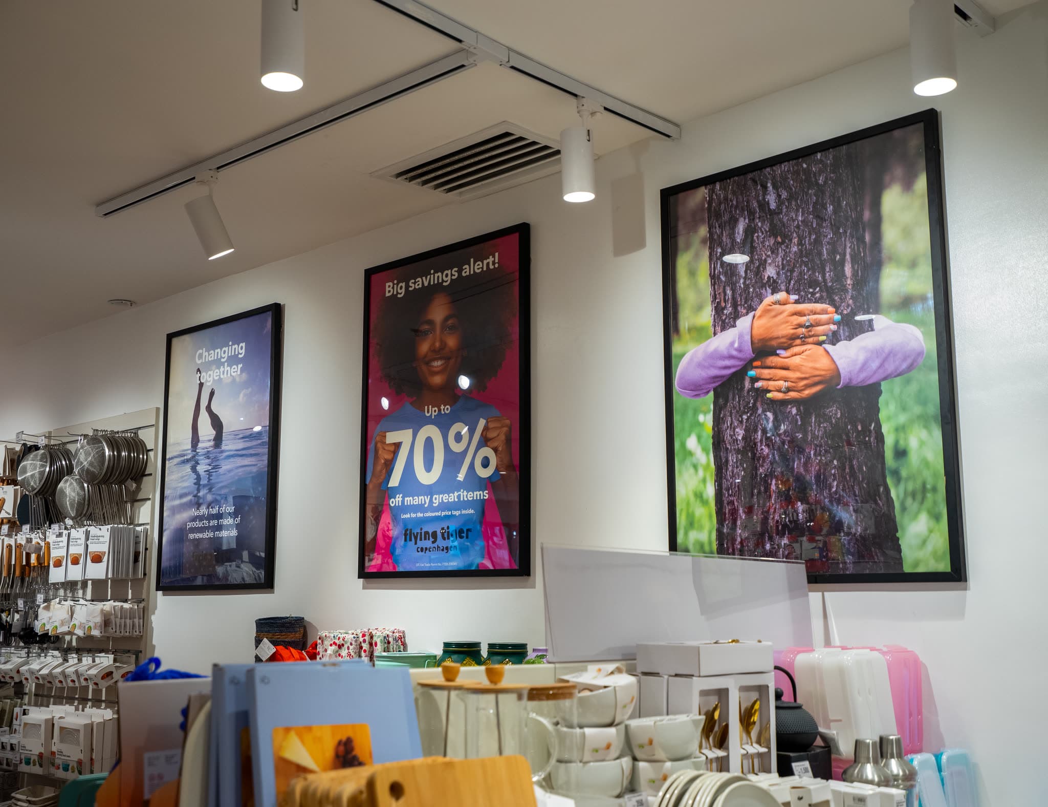 Three framed backlit poster panels installed above shelving in a retail store