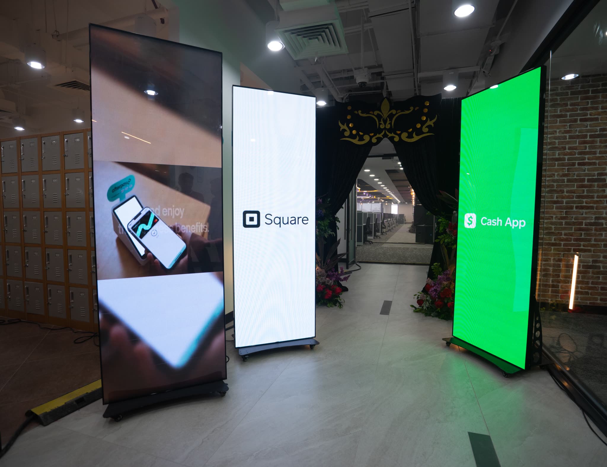 Three portrait LED totem displays running brand content in an office corridor