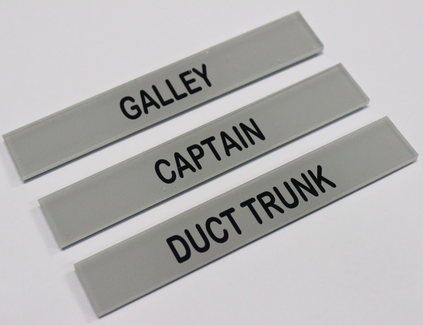 Three engraved acrylic marine labels reading Galley, Captain and Duct Trunk