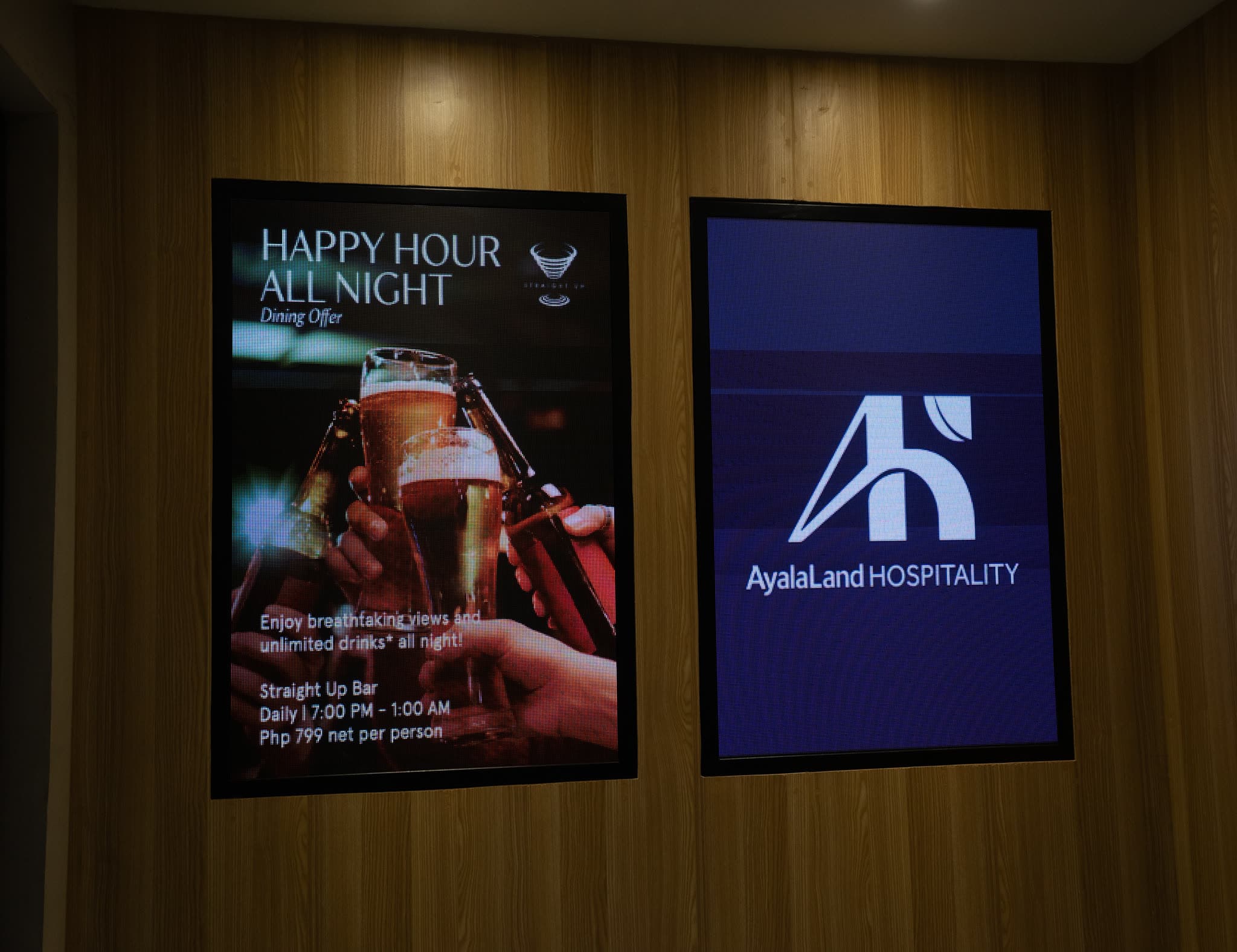 Two portrait LED poster displays mounted on a timber wall in a hotel interior